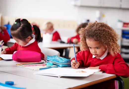 Young girl sitting in class and writing next to her favourite pencil case