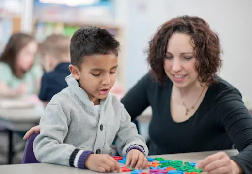 A teacher is helping a student with his toys at his table.