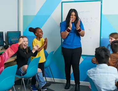 An 11 Plus Tutor stands in front of a group of children running a lesson - the children are happy and excited to have understood a tricky topic.