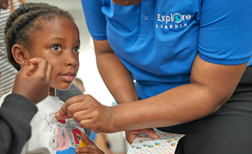 A child is receiving a sticker from a tutor.