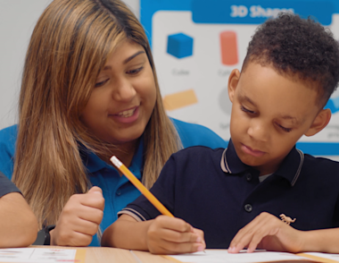 A young child is writing in a workbook with the support of an Explore Learning tutor.
